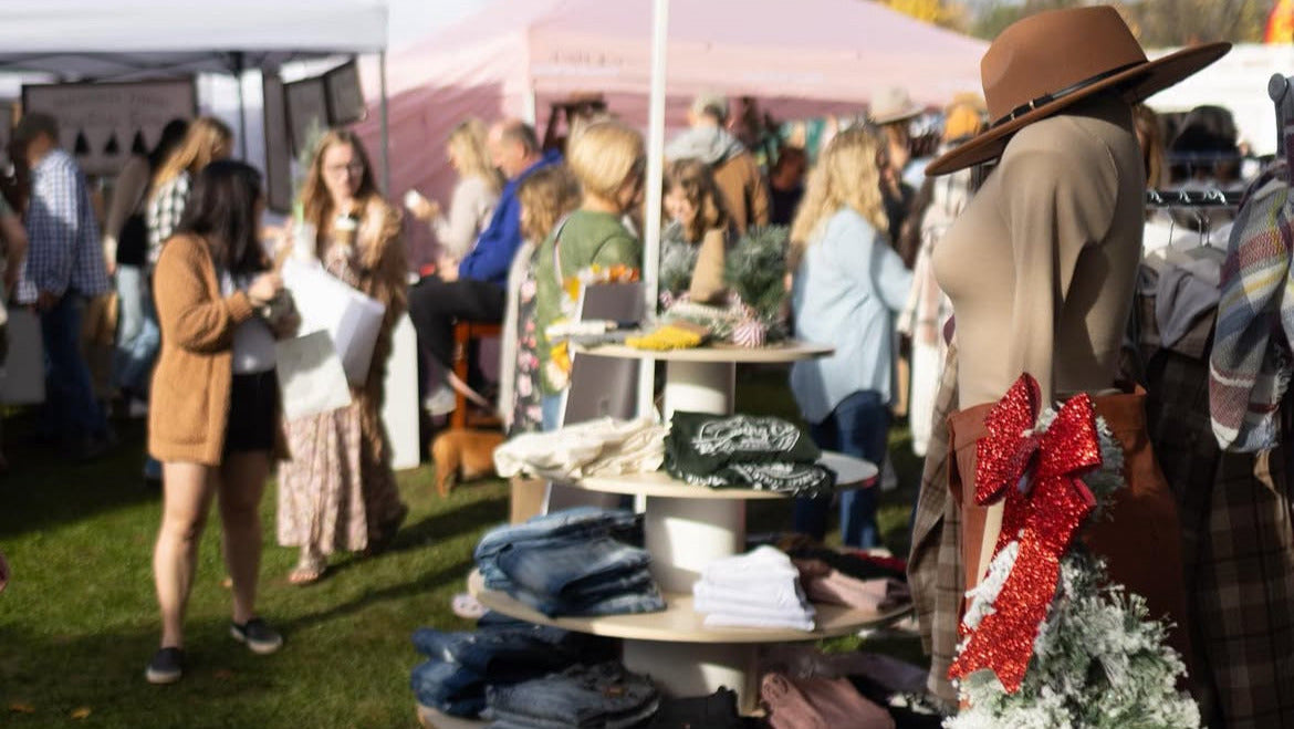 Outdoor market scene with people and a vendor table displaying clothing and accessories.