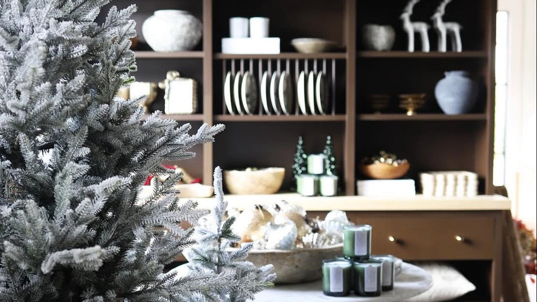 Decorative interior with a flocked Christmas tree and a bookshelf filled with various items.